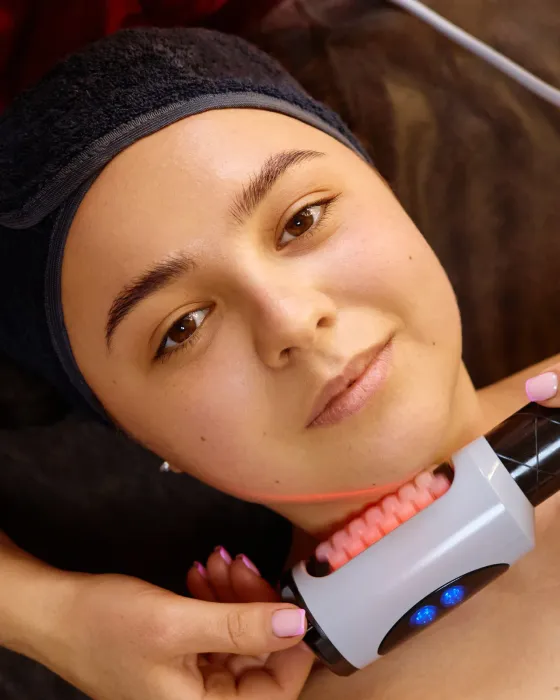 A handheld treatment device being worked along a client’s jaw and neck during a session