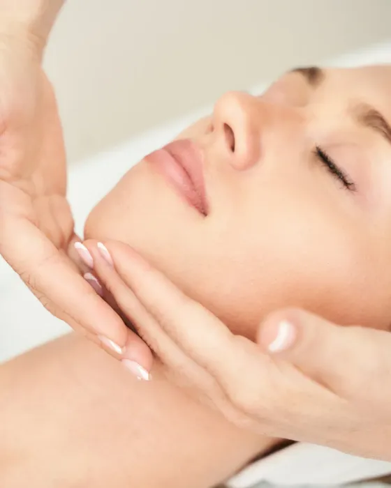 Hands performing a lymphatic facial massage on a relaxed face during a treatment